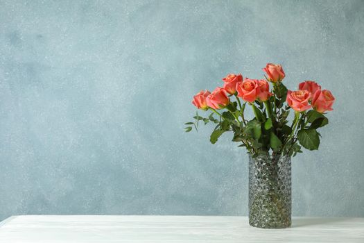 Vase with orange roses on white table against light background, space for text