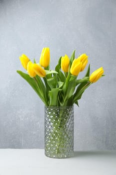 Beautiful yellow tulips in a glass vase on wooden table