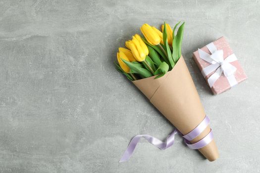 Beautiful bouquet of yellow tulips with gift on grey background, top view. Space for text