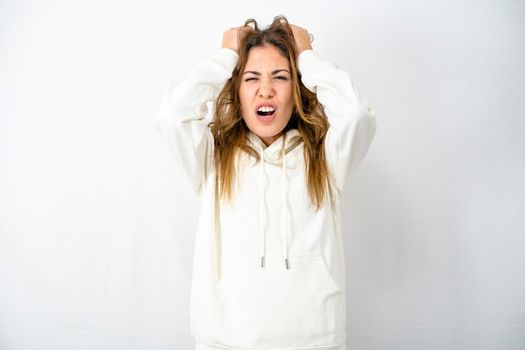 Young model isolated on white background tears hair out with despair face expressing anger by screaming with her mouth open and closed eyes. Concept of modern times stressed and frustrated woman