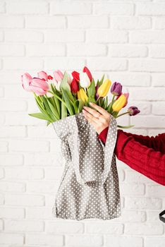 Eco friendly, zero waste concept. Spring shopping. Woman hand holding gray polka dot fabric bag with colorful tulips