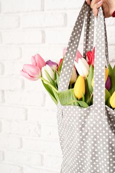 Eco friendly, zero waste concept. Spring shopping. Woman hand holding gray polka dot fabric bag with colorful tulips