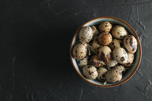 Many quail eggs in bowl on black background, space for text and top view