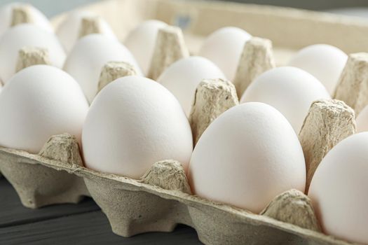 White chicken eggs in carton box on wooden table, space for text and closeup