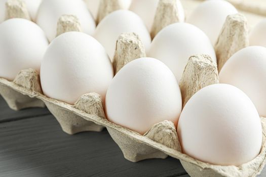 White chicken eggs in carton box on wooden table, space for text and closeup