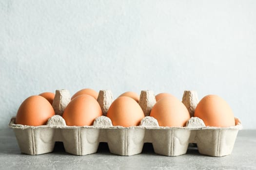 Chicken eggs in carton box on gray background, space for text