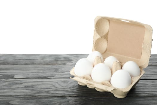 Few raw chicken eggs in carton box on wooden table against white background