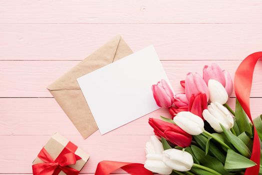 Frame mock up with Greeting card and envelope with colorful spring tulips top view over pink wooden background. Flat lay, top view.