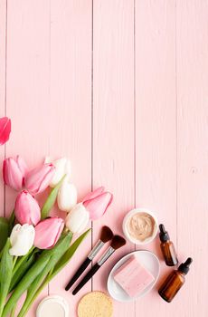 Top view of cosmetics with pink and white tulips top view flat lay on pink wooden background, flat lay