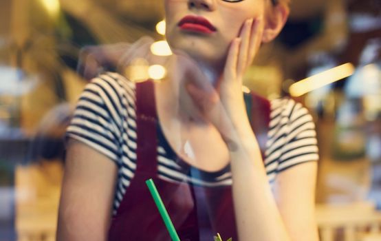 fashionable woman in red sundress sits in a cafe and mirror glass reflection of cars on the street. High quality photo