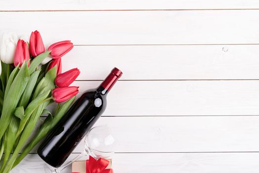 Valentines day concept. Bunch of colorful tulips and wine bottle on white wooden background