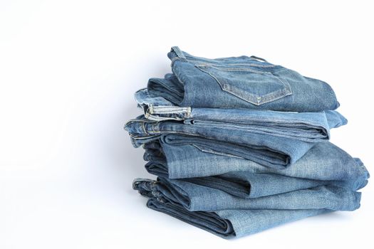 Stack of jeans pants on white background, space for text