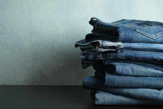 Stack of jeans pants on black table, space for text