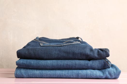 Stack of jeans pants on light pink background, space for text