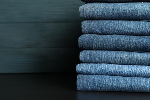 Stack of jeans pants on black table, space for text