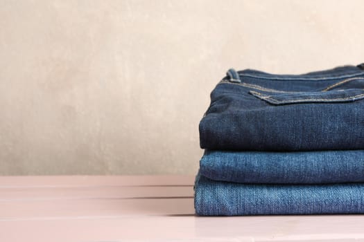 Stack of jeans pants on light pink background, space for text