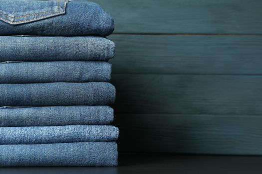 Stack of jeans pants on black table, space for text