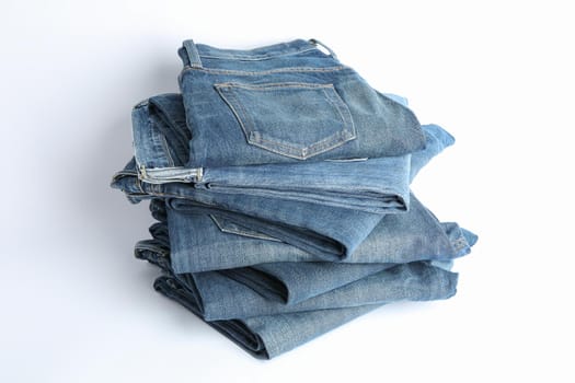 Stack of jeans pants on white background, space for text