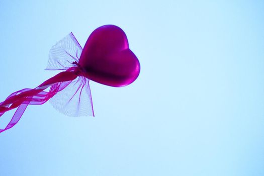 Red heart attached to a stick with a bow hanging. Copy space