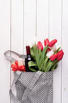 Eco friendly, zero waste concept. Gray fabric bag ful of colorful tulips and wine bottle on white wooden background