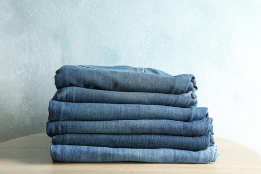 Stack of jeans pants on wooden table, space for text