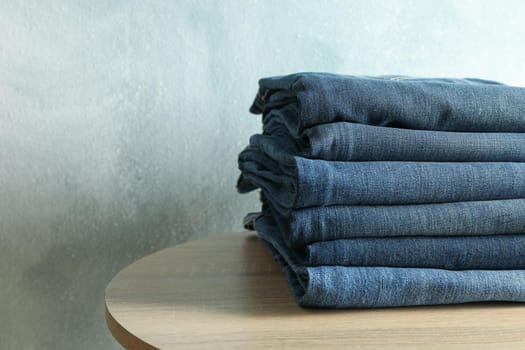 Stack of jeans pants on wooden table, space for text