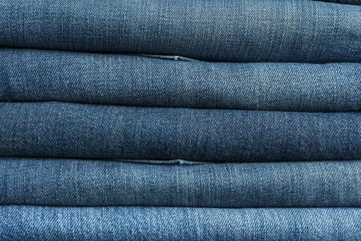 Stack of jeans pants textured background, close up