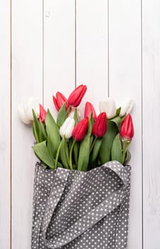 Eco friendly, zero waste concept. Gray fabric bag ful of colorful tulips on white wooden background