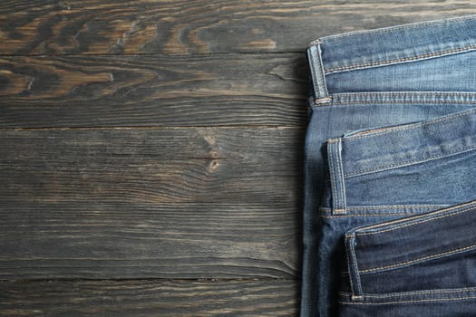 Different jeans folded on a wooden background, space for text