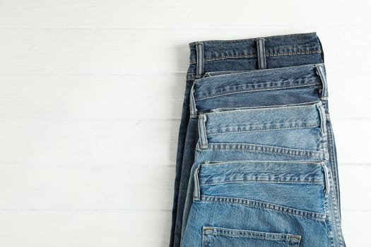 Different jeans folded on a white wooden background, space for text