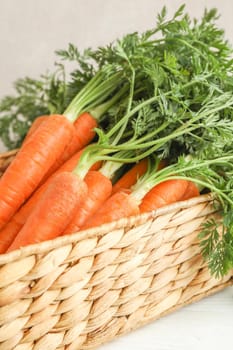 Wicker basket with ripe carrots on wooden table, closeup