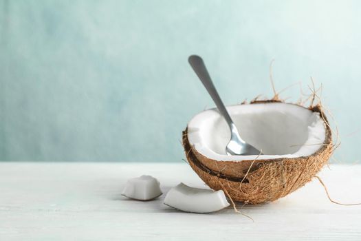 Half coconut with spoon on wooden table against grey background