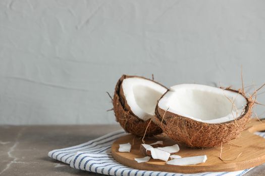 Cutting board with split coconut on table against grey background