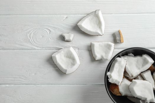 Plate with coconut pieces on white wooden background, space for text