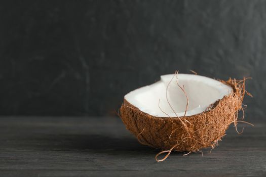Half tropical coconut on wooden table against black background, space for text