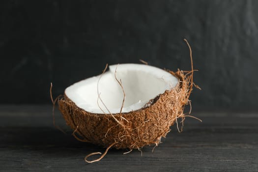 Half tropical coconut on wooden table against black background, space for text