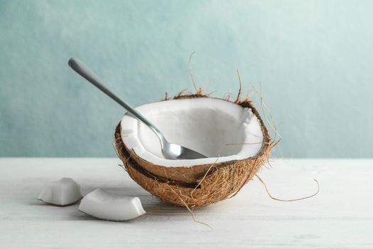 Half coconut with spoon on wooden table against grey background