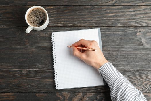 Man hand with pen, copybook and cup of coffee on wooden background