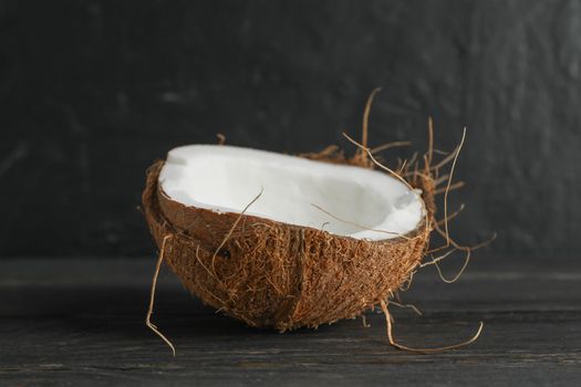 Half tropical coconut on wooden table against black background, space for text