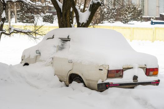 Stuck cars under the snow and ice. City street after blizzard. Buried vehicle in snowdrift on the road. Parking lots in winter after heavy snowfall. Uncleaned roads. Record-breaking amounts of snow.