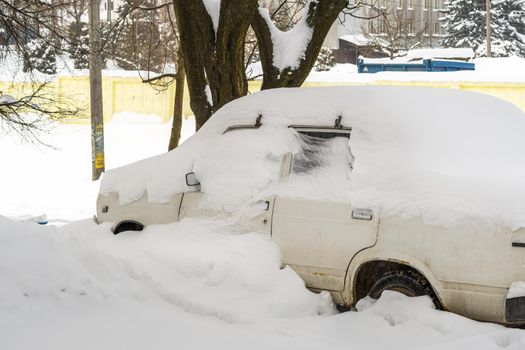 Stuck cars under the snow and ice. City street after blizzard. Buried vehicle in snowdrift on the road. Parking lots in winter after heavy snowfall. Uncleaned roads. Record-breaking amounts of snow.