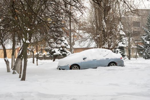 Stuck cars under the snow and ice. City street after blizzard. Buried vehicle in snowdrift on the road. Parking lots in winter after heavy snowfall. Uncleaned roads. Record-breaking amounts of snow.