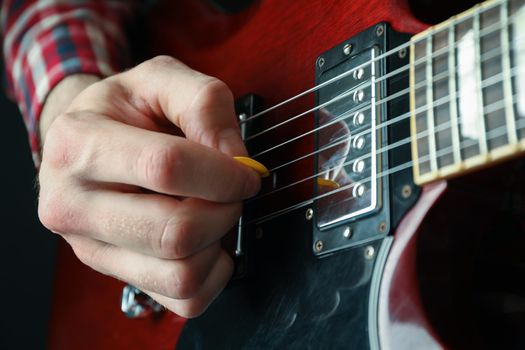 Man playing on electric guitar against dark background, closeup