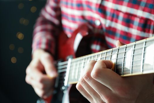 Man playing on electric guitar against dark background with blurred lights