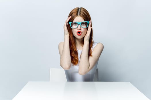 pretty red-haired woman sitting at the table wearing blue glasses red lips . High quality photo