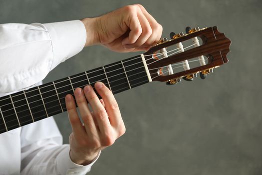 Man tunes classic guitar against dark background, space for text