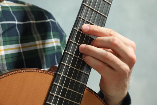 Man playing on classic guitar against light background, closeup