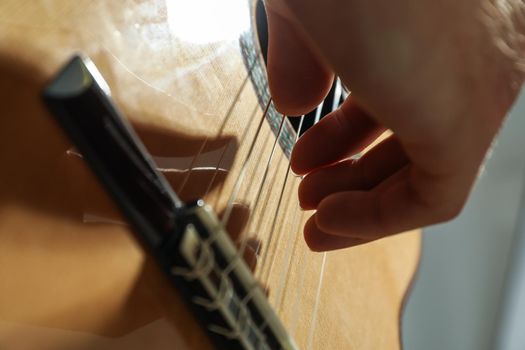 Man playing on classic guitar against light background, closeup