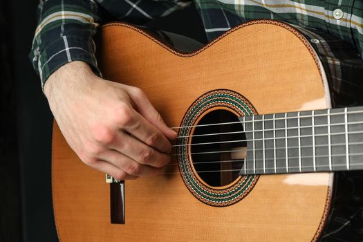 Man playing on classic guitar against dark background, space for text