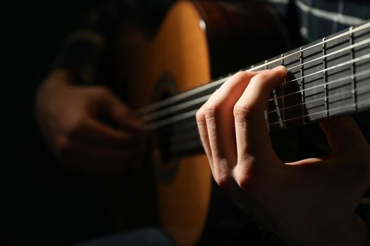 Man playing on classic guitar against dark background, closeup